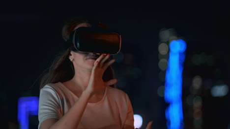 A-young-woman-in-virtual-reality-glasses-in-the-night-city-moves-her-hands-mastering-the-application-interface.-VR-technologies-of-the-future-in-everyday-life.-Virtual-reality-games